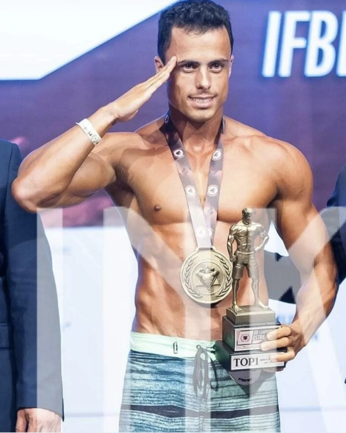 Guilherme Leal batendo continência no pódio de um campeonato da IFBB, com a medalha