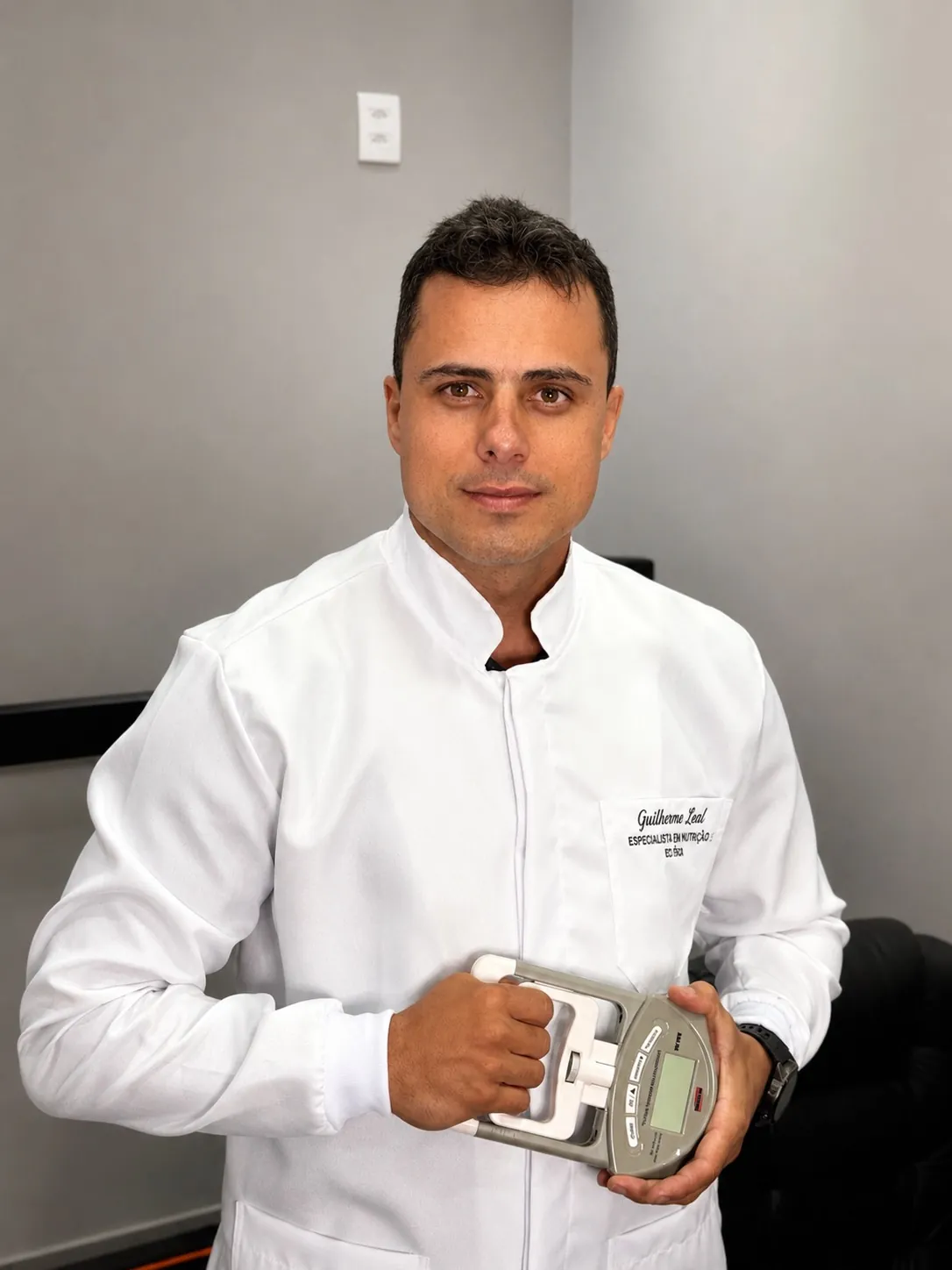 Guilherme Leal de jaleco branco segurando um dinamômetro, aparelho que mede a força da mão