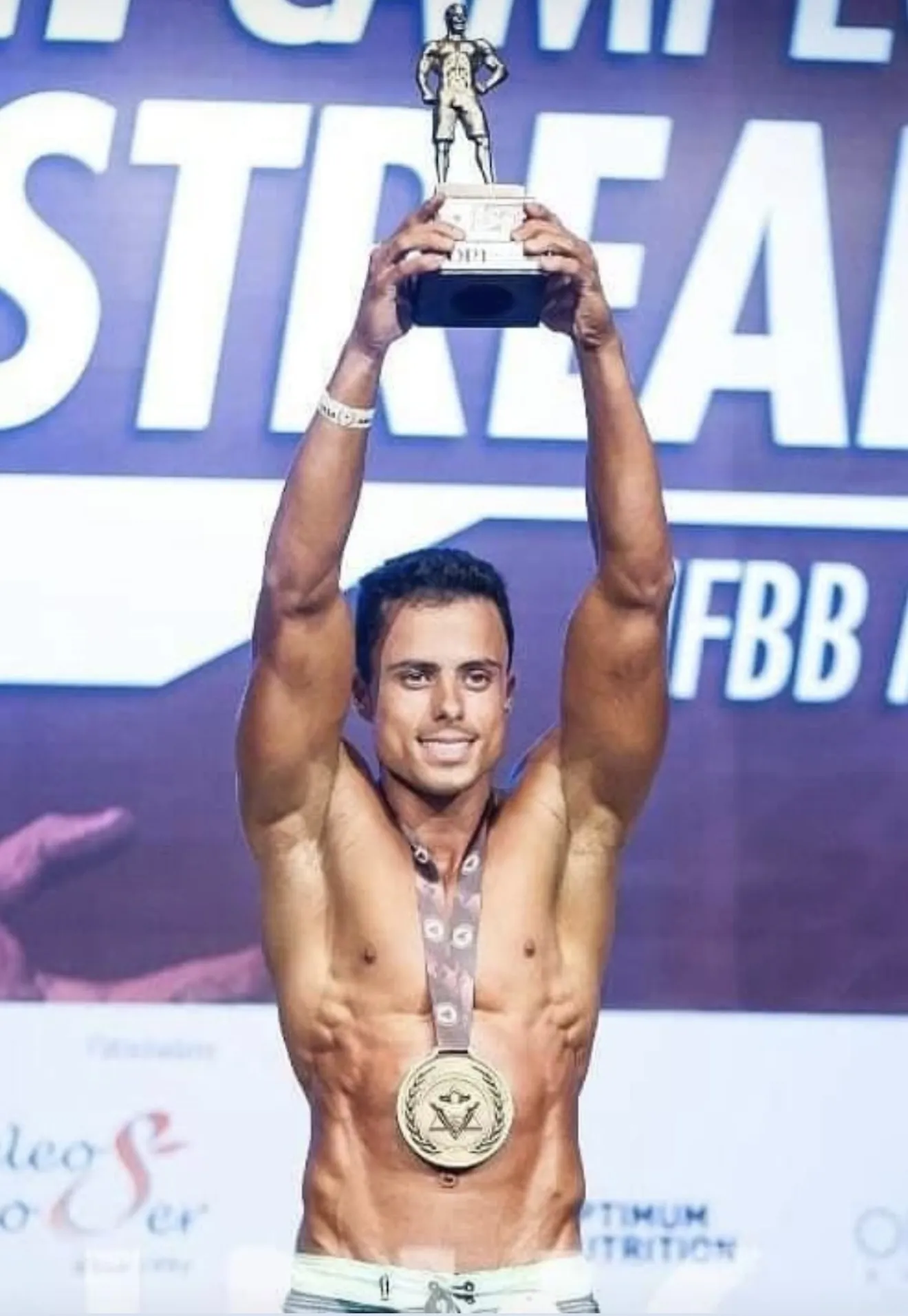 Guilherme Leal no pódio de um campeonato de fisiculturismo da IFBB, erguendo o troféu